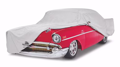 A red classic car partially covered with a gray car cover
