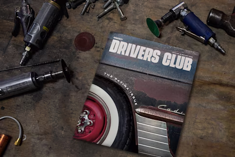 “Drivers Club” magazine featuring a rusty classic car and whitewall tire, placed on a workshop table with tools.