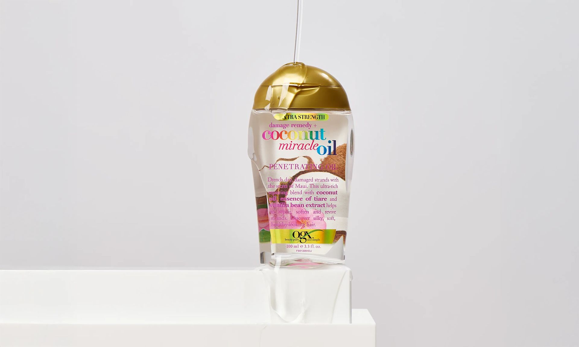 OGX® Coconut Miracle Oil Penetrating Oil being poured over a bottle of Miracle Oil