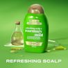 Vue avant du revitalisant extra fort romarin et menthe OGX® de 385 mL avec une éprouvette et une bouteille