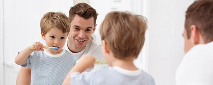 Photo of dad helping son brush his teeth