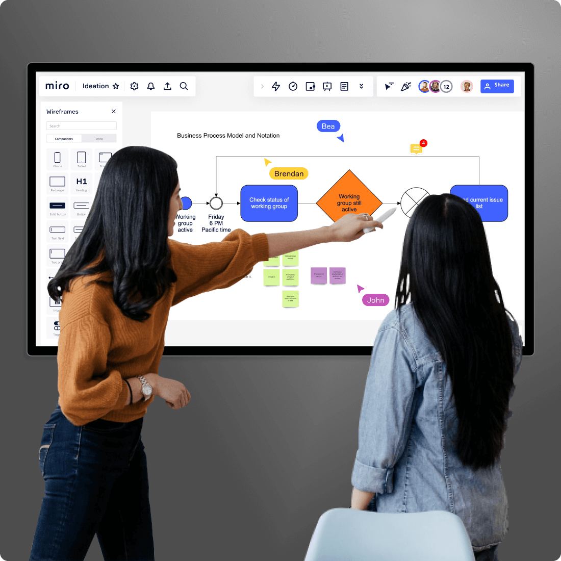 2 personnes devant un écran interactif qui affiche un tableau Miro