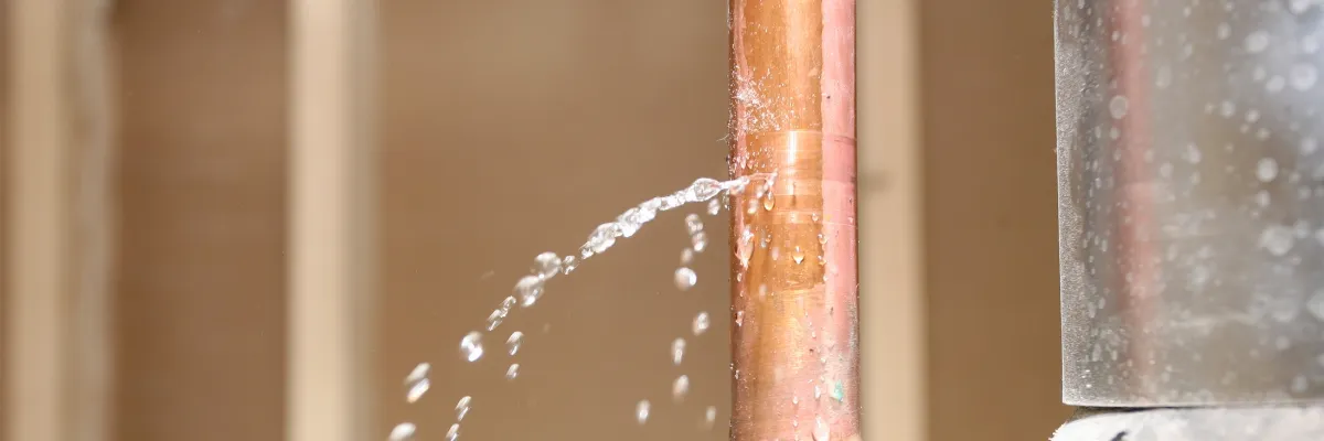 A copper pipe with a leak, squirting water.
