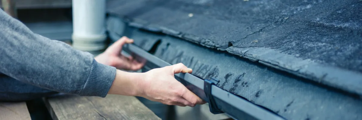 A person fitting a black rain gutter.