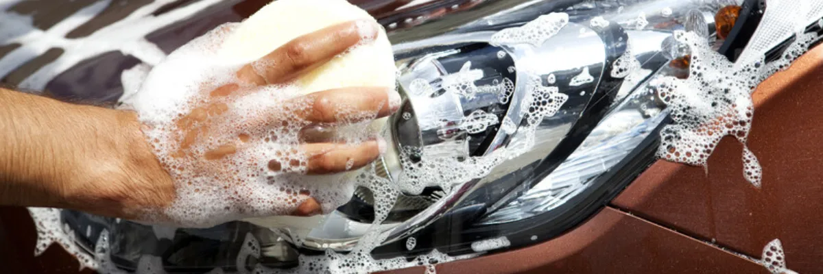A close-up of a man washing a brown car with a soapy sponge.