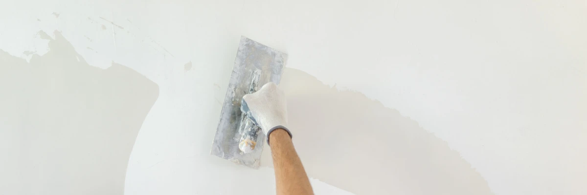 A person skimming a white wall with plaster.