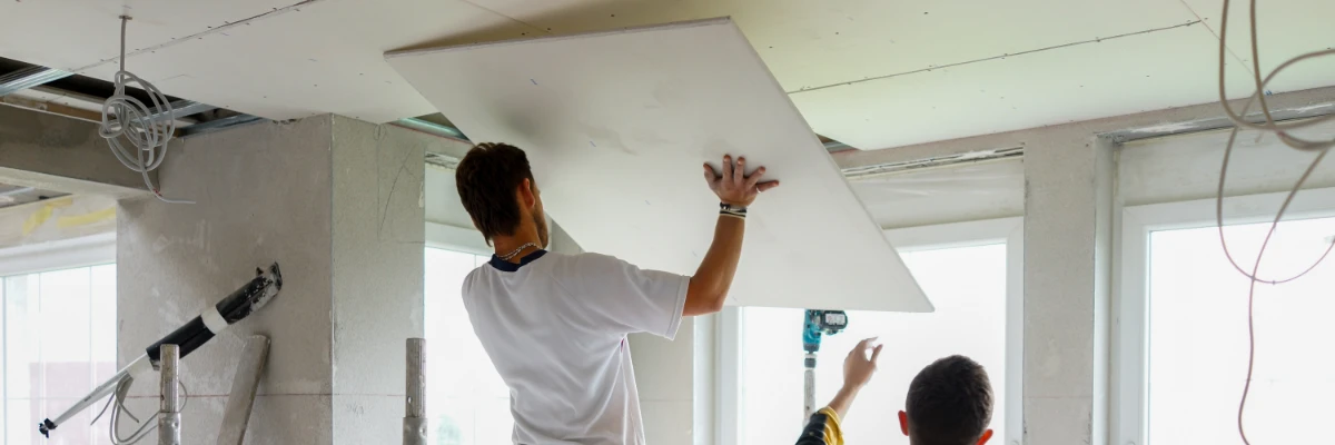 A contractor holding a piece of plasterboard up towards the ceiling, ready for installation.