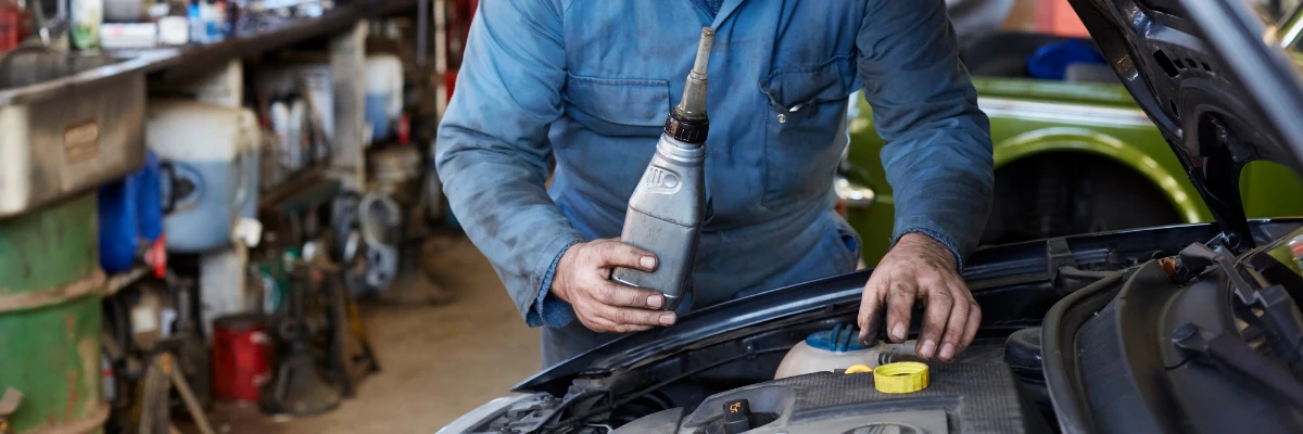 A mechanic preparing pour engine oil into a car's engine.