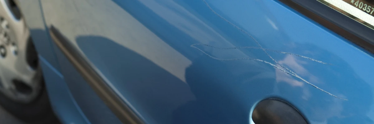A blue car's paintwork with several scratches.