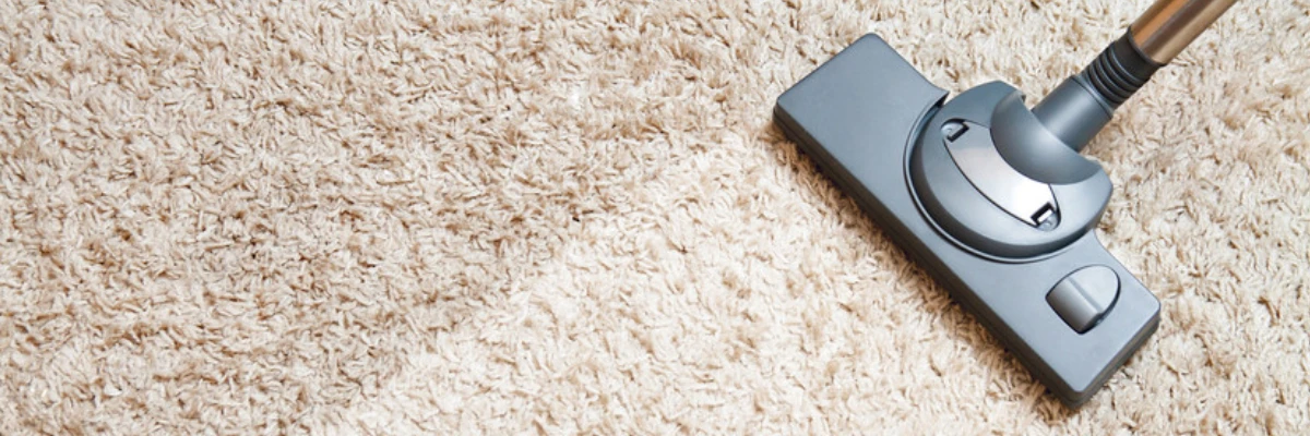 A vacuum cleaner running over a beige carpet.