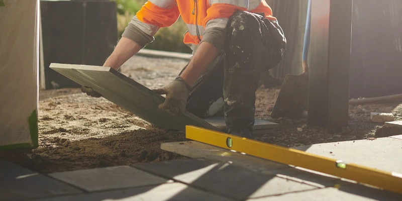 How Long Does Cement Take to Dry? Factors and Timelines Article Image A builder laying a paving slab on a cement foundation.
