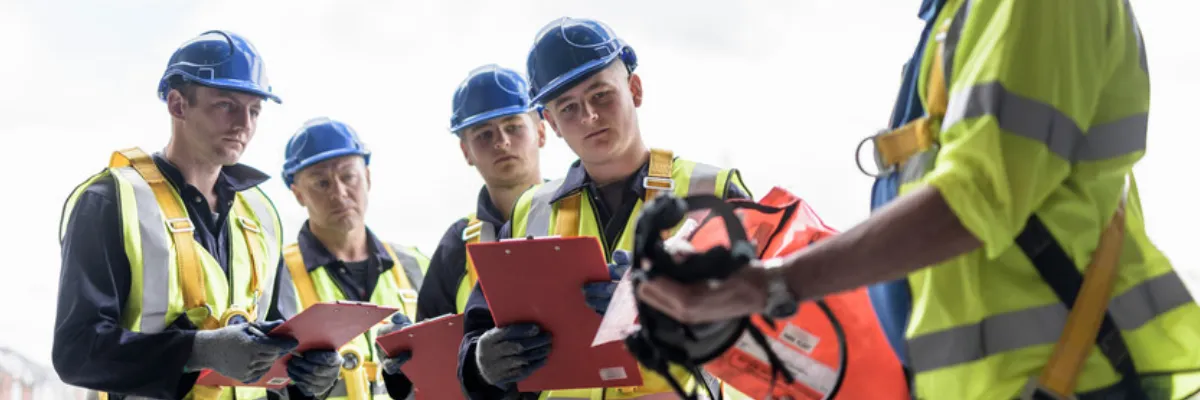 A tradesperson giving instruction to a group of apprentices holding clipboards.