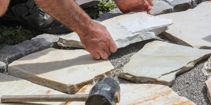 How to Lay a Patio Without Cement: Alternatives Explained Article Image Stone paving slabs being laid over an aggregate foundation.