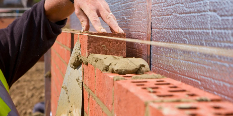 How to Lay Bricks: A Beginner’s Guide Article Image 2 A bricklayer neatening up mortar on a partly constructed brick wall.