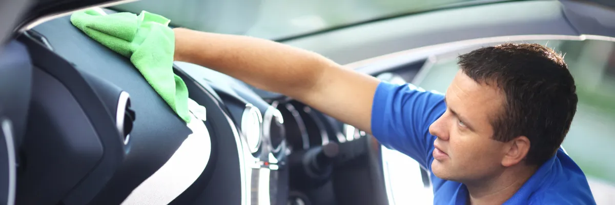 A man cleaning a car's dashboard with a microfibre cloth.