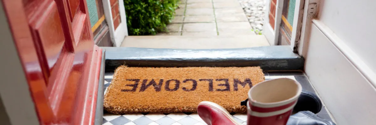 A welcome mat next to some wellies by an open red front door.