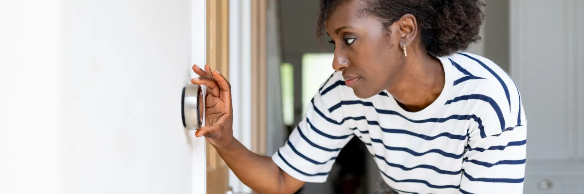 A woman adjusting a smart thermostat.