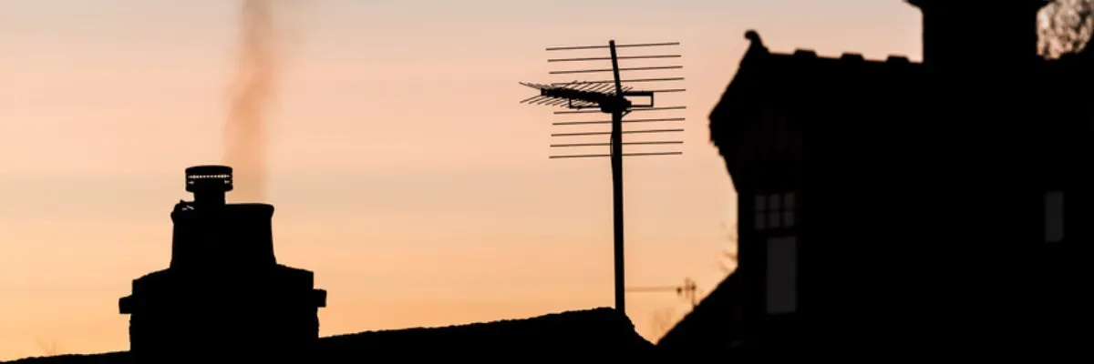A silhouette of a TV aerial on a roof with a sunset in the background.