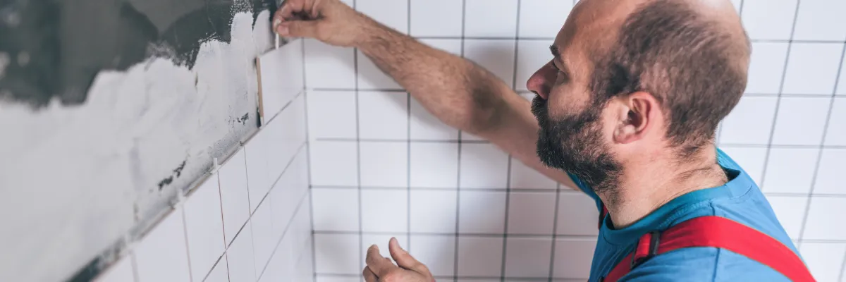 A tiler placing a white tile against a wall using tile adhesive.