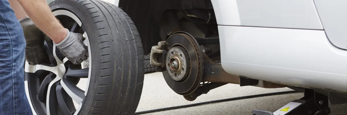 A mechanic removing a tyre to access a car's brake disc and pad.