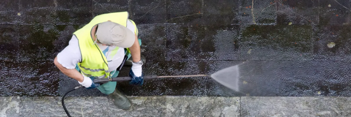 A man power washing a grey stone patio.