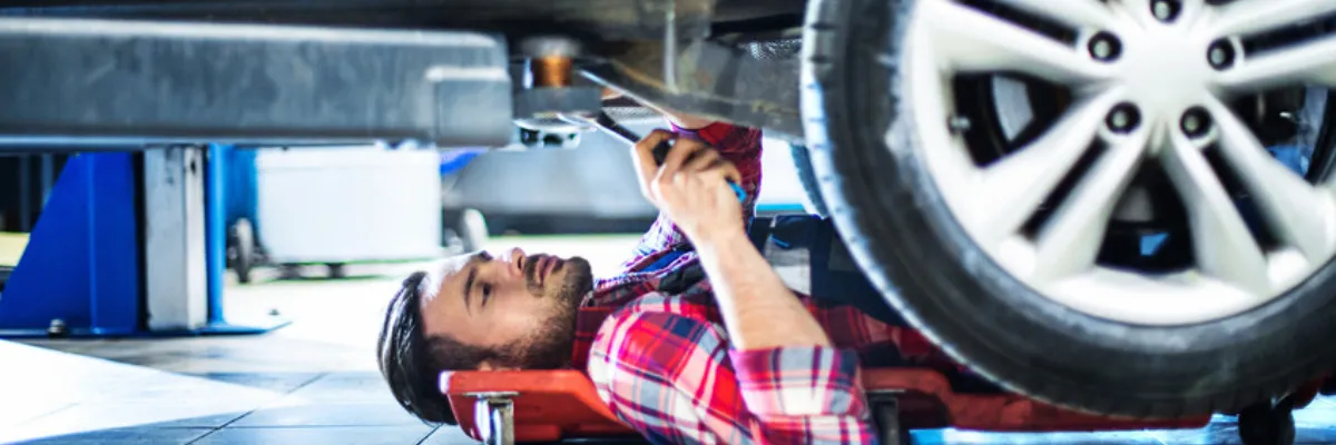 A mechanic inspecting a vehicle from below.
