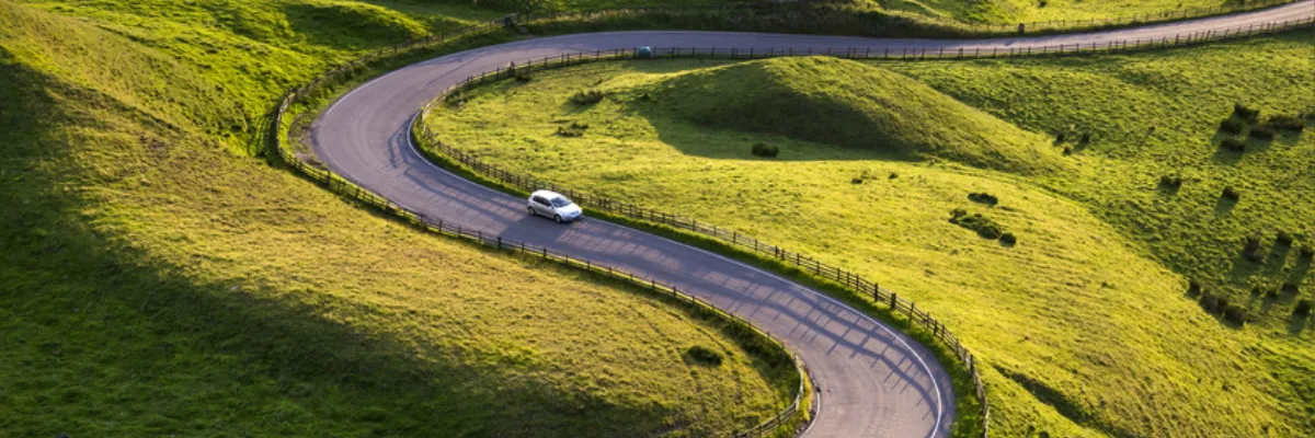 A white car driving on a windy chicane surrounded by grassy fields.