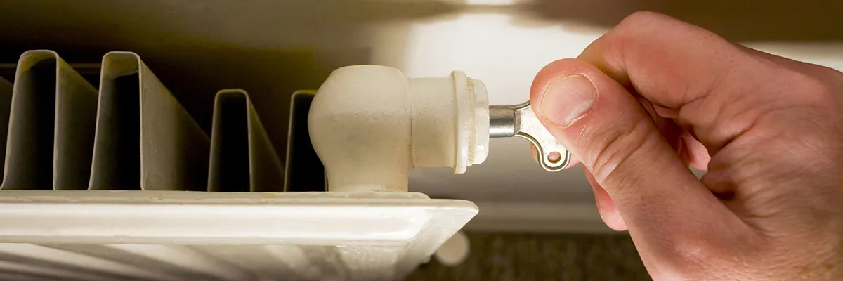 A person turning a radiator key in a radiator valve.
