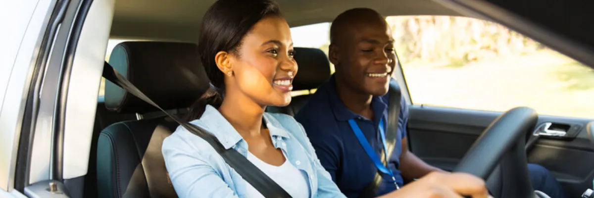 A male driving instructor teaching a female learner in a car.