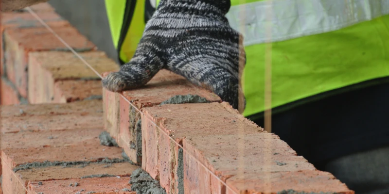 How to Lay Bricks: A Beginner’s Guide Article Image A bricklayer placing a brick on a partly constructed brick wall.