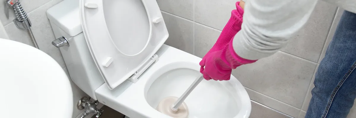 A person using a plunger to clear a blocked toilet.