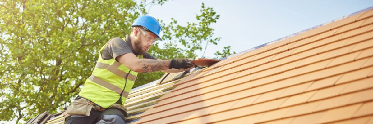 A roofer adding roof tiles to a new roof structure.