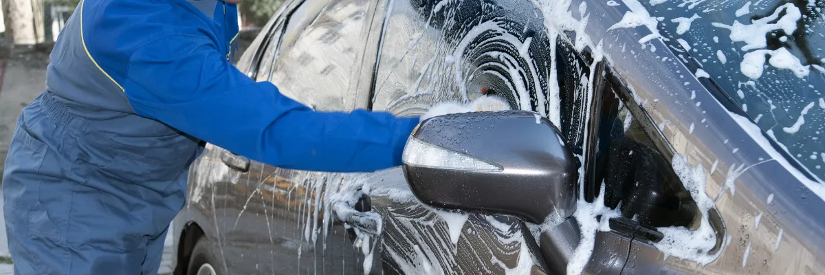 A person cleaning a car's windows with soap.