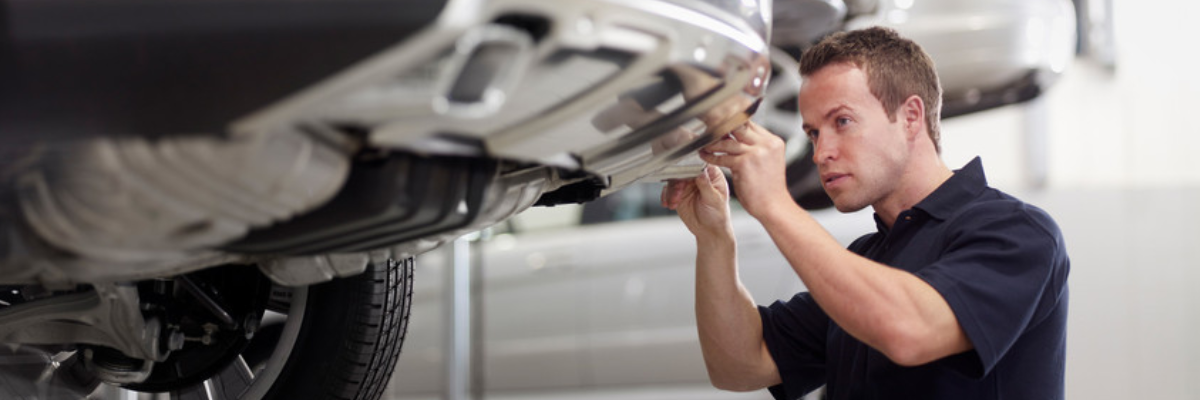 A mechanic examining a silver car that has been jacked up.