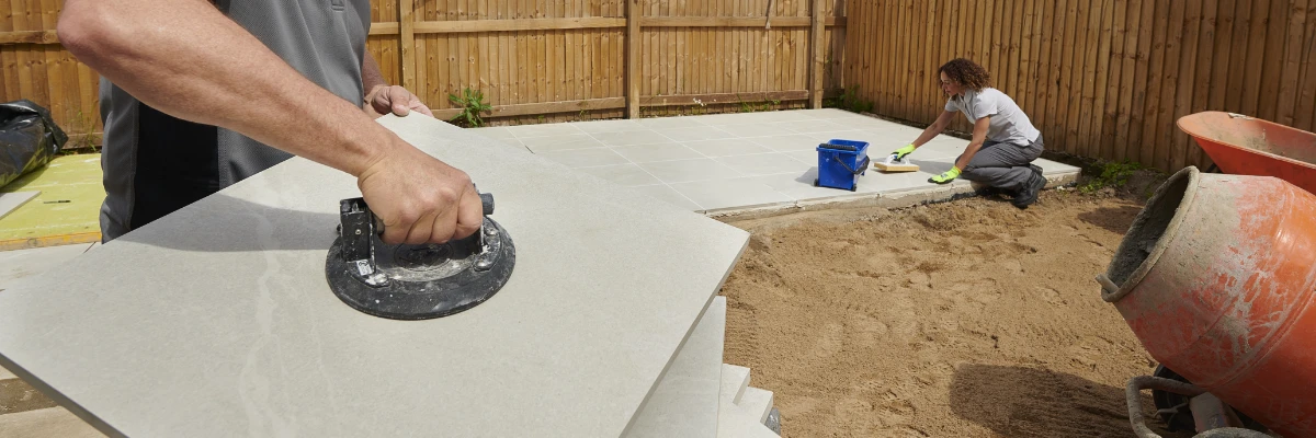 A person holding a paving slab, preparing to lay the slab.