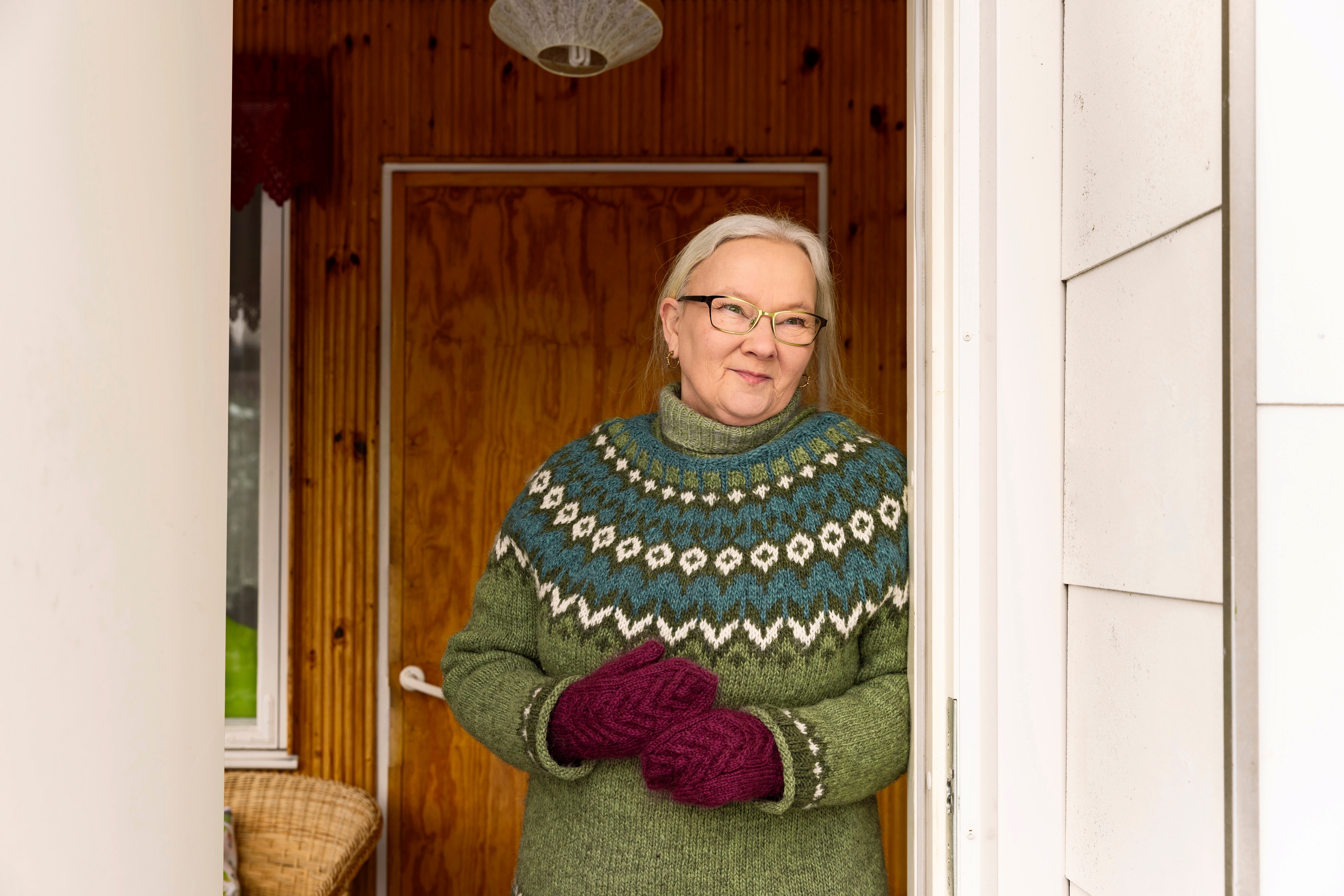 nainen seisoo oviaukossa villapaita yllään