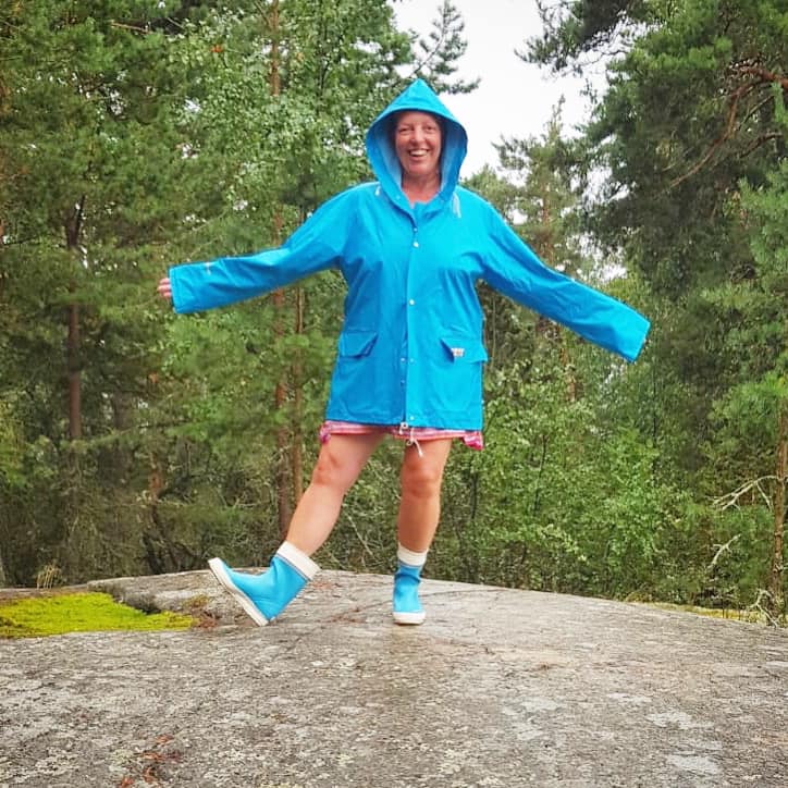 nainen seisoo kalliolla turkoosissa sadetakissa.