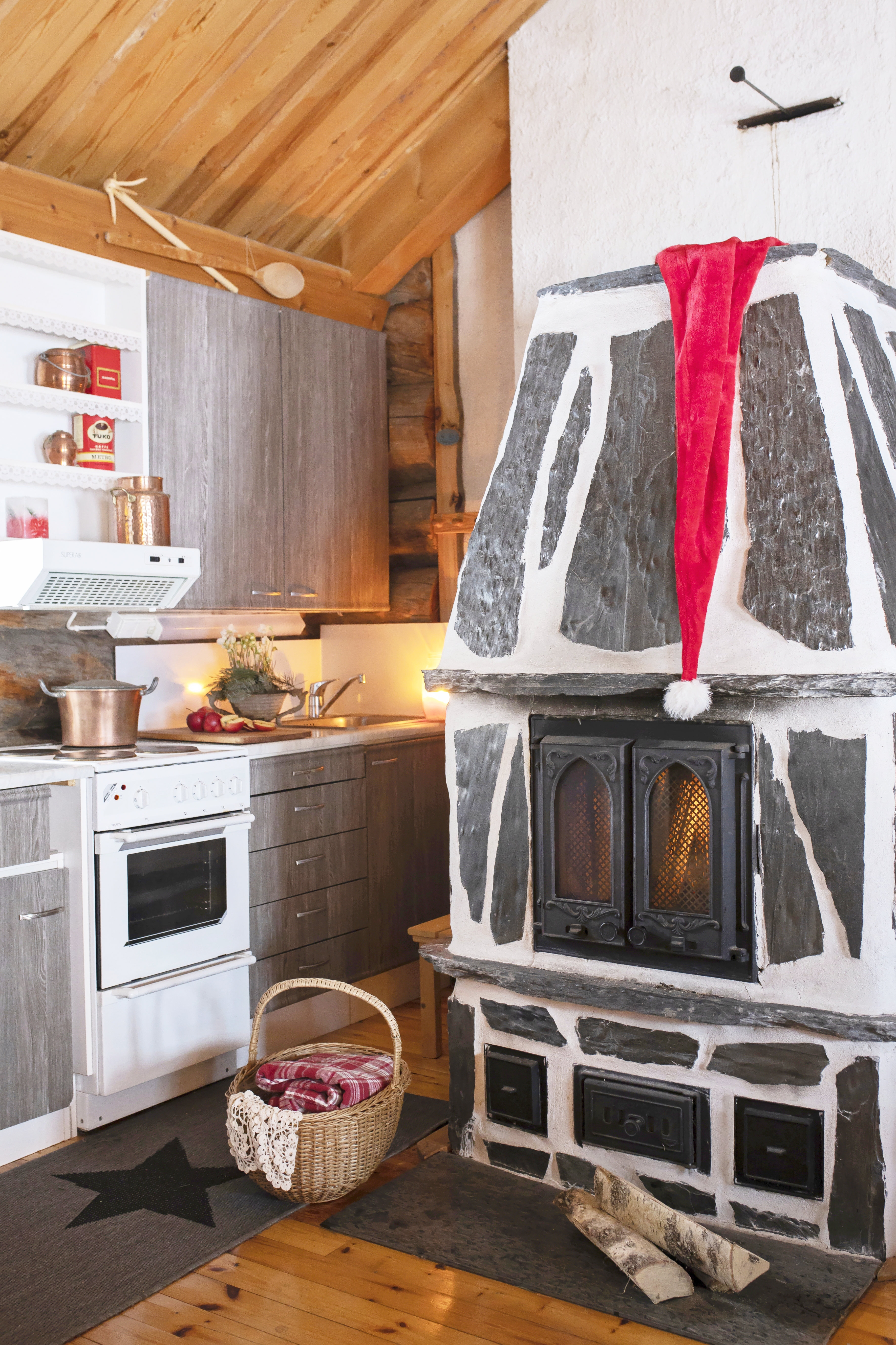 Vuolukivitakassa tonttulakki roikkumassa ja mökin keittiö.