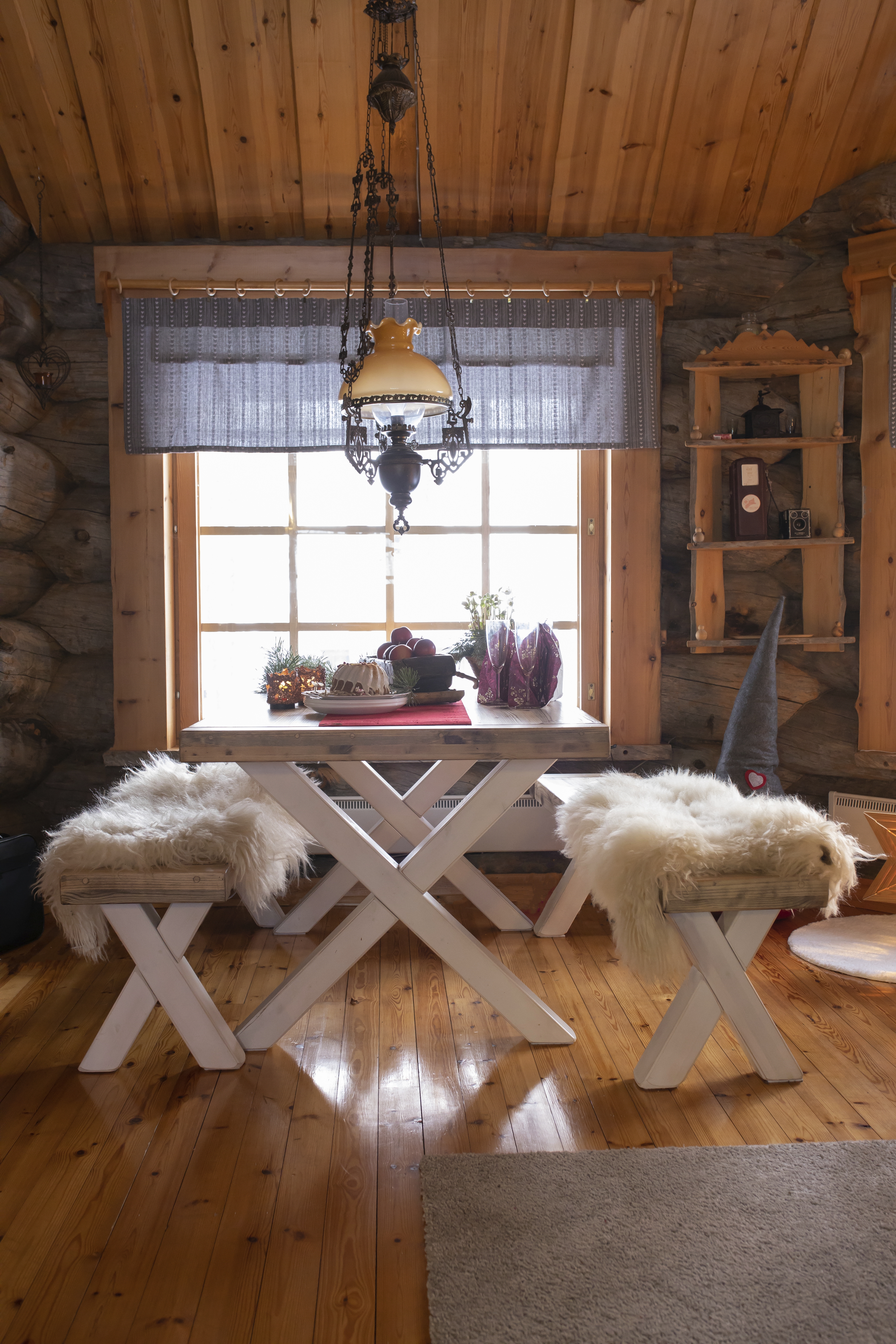 Taljat pirtinpenkeillä, pöytä ja ikkuna, öljylamppu ja seinäkaappi.