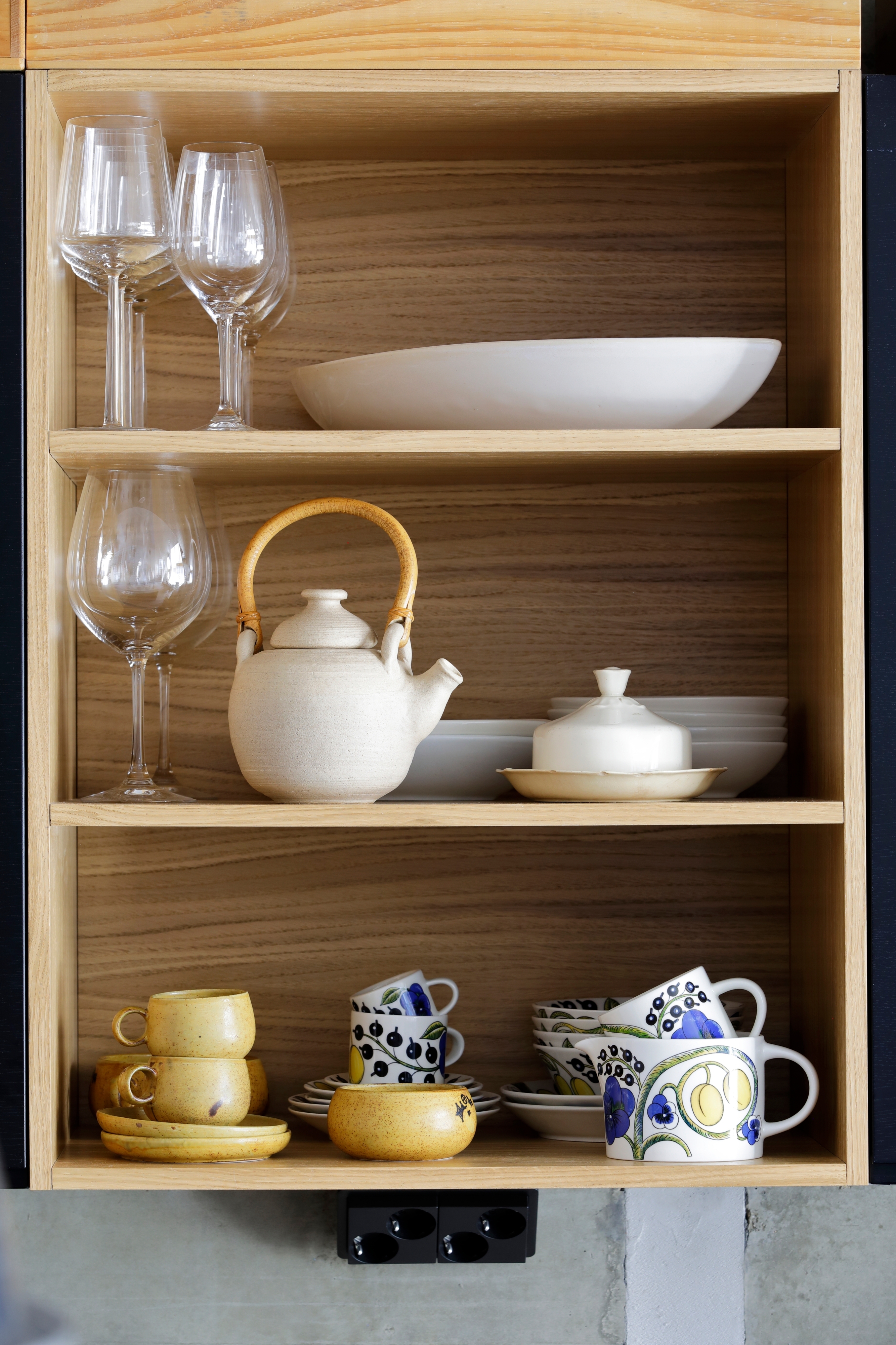 An oak-veneered open shelf showcasing dishes from Pentik’s Hiisi and Birger Kaipianen’s Paratiisi series