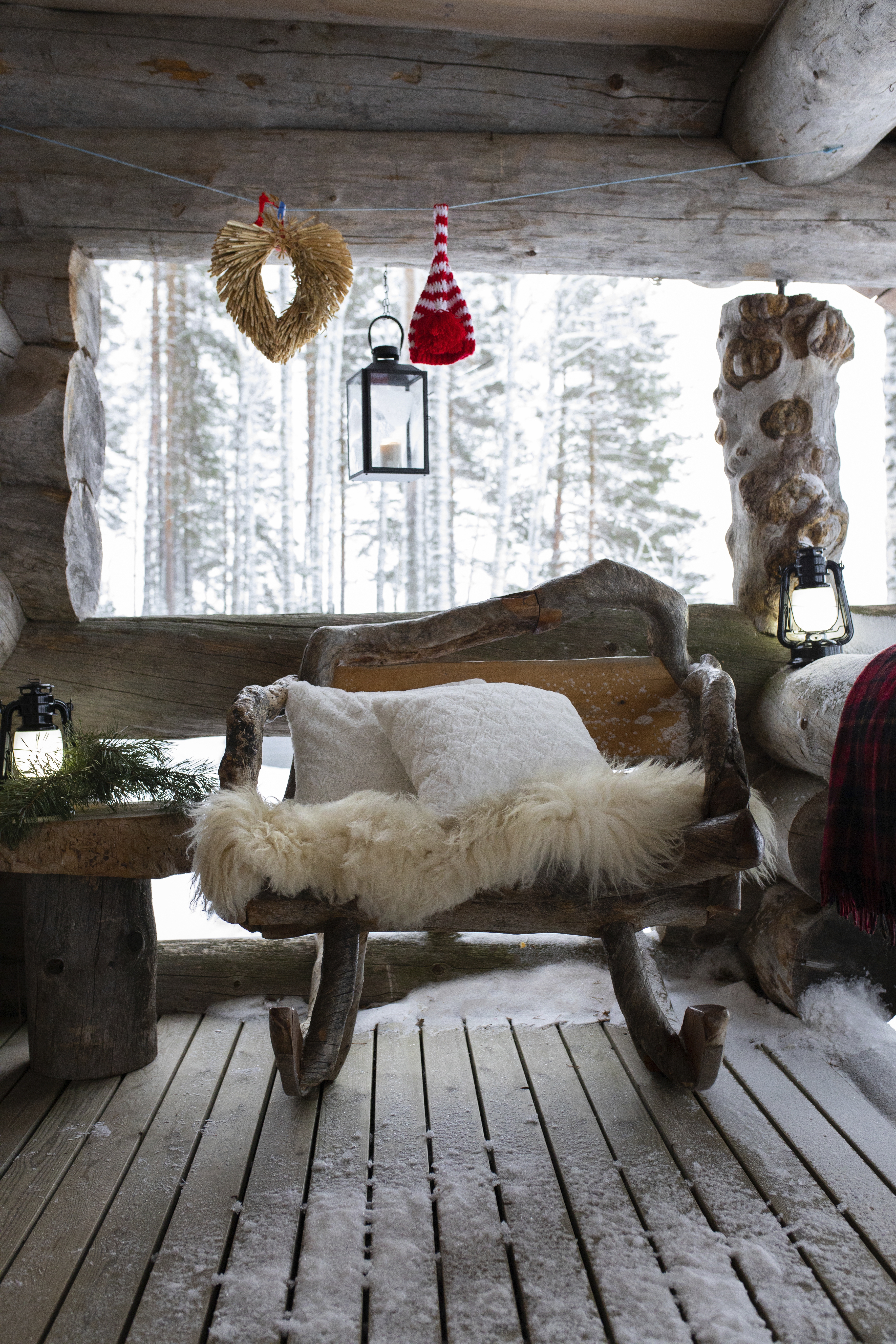 Lumisen mökin terassilla kelohonkainen keinu, jolla on lampaantalja.