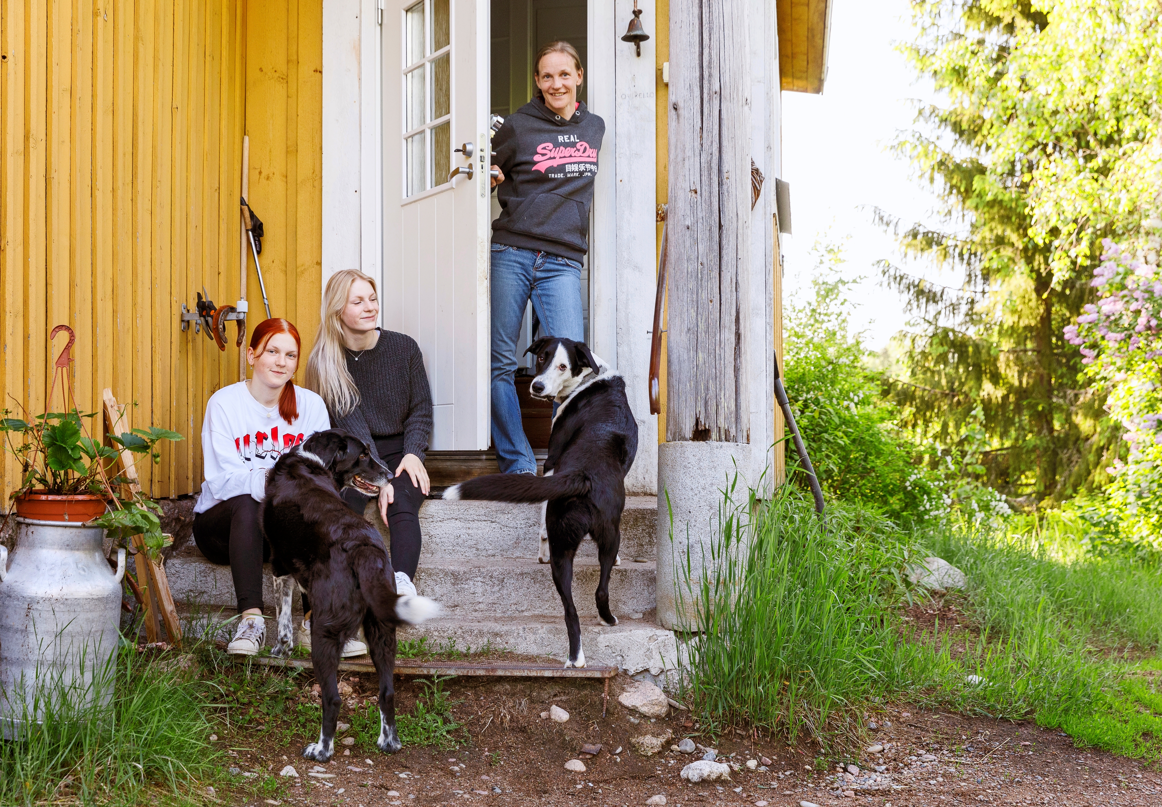 Äiti ja tyttäret sekä kaksi koiraa kodin portailla