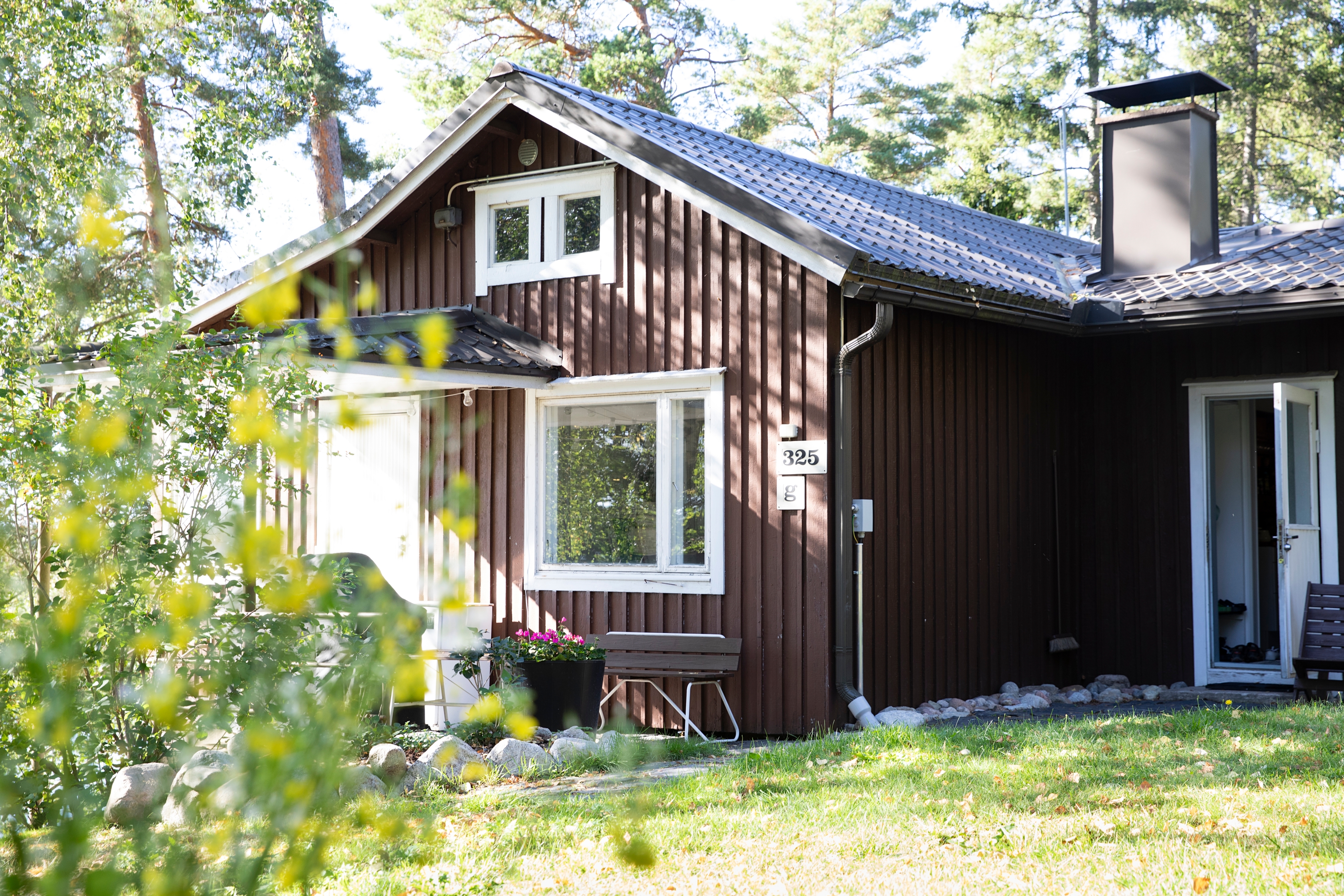 Ruskea kesämökki ulkokuvassa, pihalla kasveja.