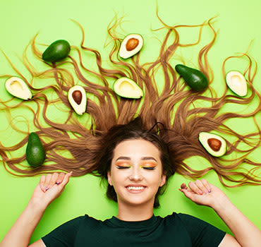 Happy funny girl lying on colored background with avocado fruits on long hair, young woman smiling, female cheerful