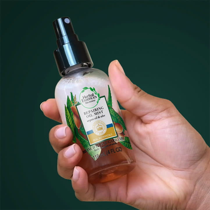 Female hand holding argan oil and aloe hair oil bottle