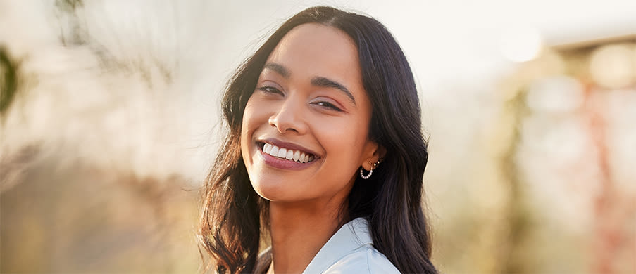 Woman with long dark brown hair smiling in front of an unfocused brown and green background