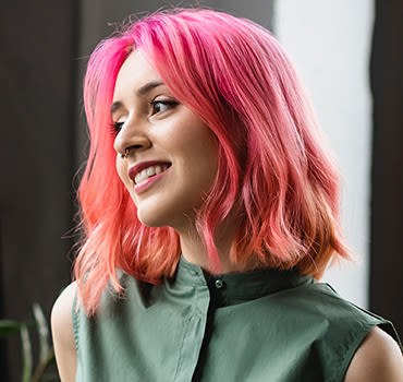 Woman with short hot pink colored hair looking to her right while holding a coffee cup