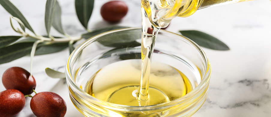 Pouring with jojoba oil from jug into bowl on white marble table