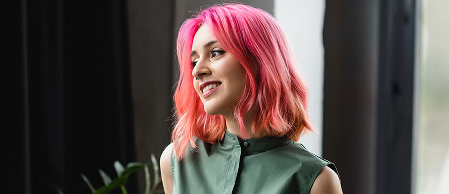Woman with short hot pink colored hair looking to her right while holding a coffee cup 