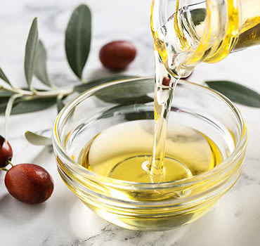 Pouring with jojoba oil from jug into bowl on white marble table